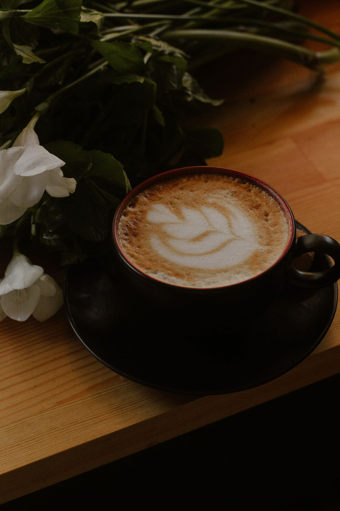 Une tasse de café avec des fleurs blanches sur une table en bois